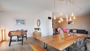 A modern dining area with a wooden table, benches, and clear chairs. There is a foosball table, a vase with flowers, and a wall-mounted mirror. - La Villa Maxine, sea view and spa (Criel-sur-Mer)