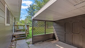 Ett takförsett utomhusområde med ett trädäck, en gång av betong och en garageport.