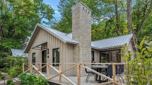 A cabin with a deck, a chimney, and a dining area.