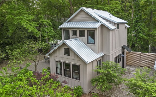 A two-story house with a deck, surrounded by trees.