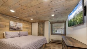 A bedroom with a wooden ceiling, a bed with a quilted cover, a wooden dresser, a window with blinds, and a painting on the wall. - Cute 3 Bedroom 2 Bath and ONLY 5 Minutes to Pigeon Forge (Pigeon Forge)