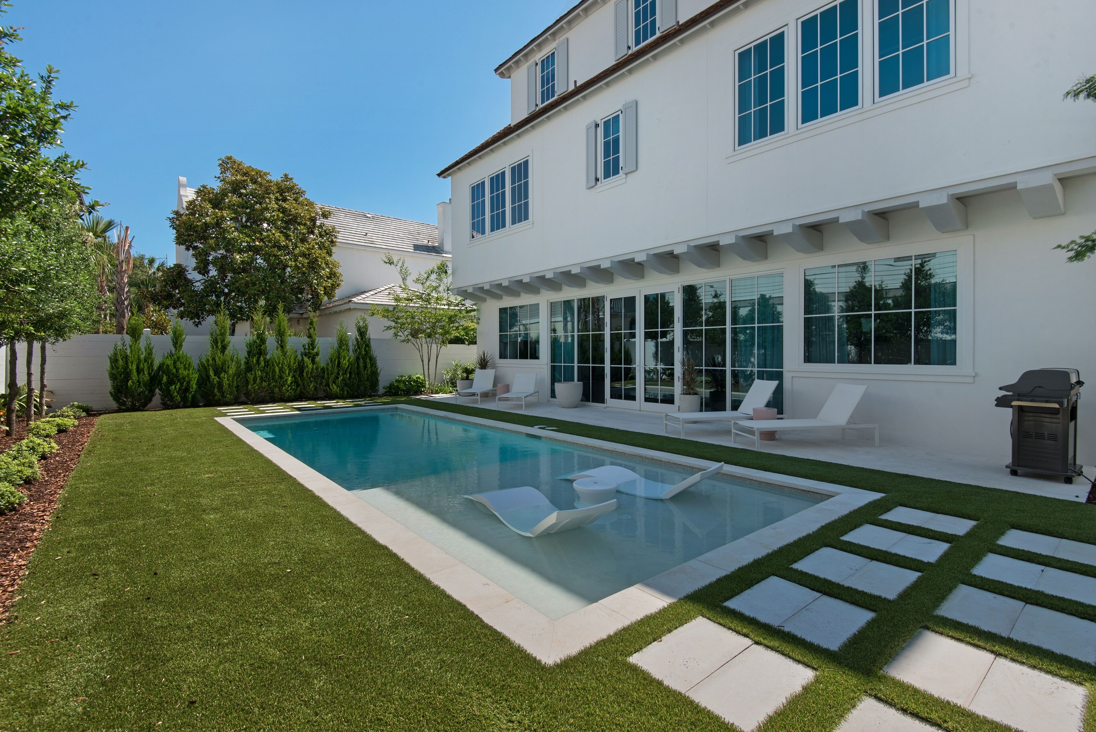 A modern house with a swimming pool, white exterior, and a well-maintained lawn.