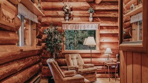 A log cabin interior with a sofa, a lamp, and a window overlooking greenery. - 11sl - Wi-fi - No Pets Log Cabin - Sleeps 7 2 Bedroom Cabin by RedAwning (Deming)