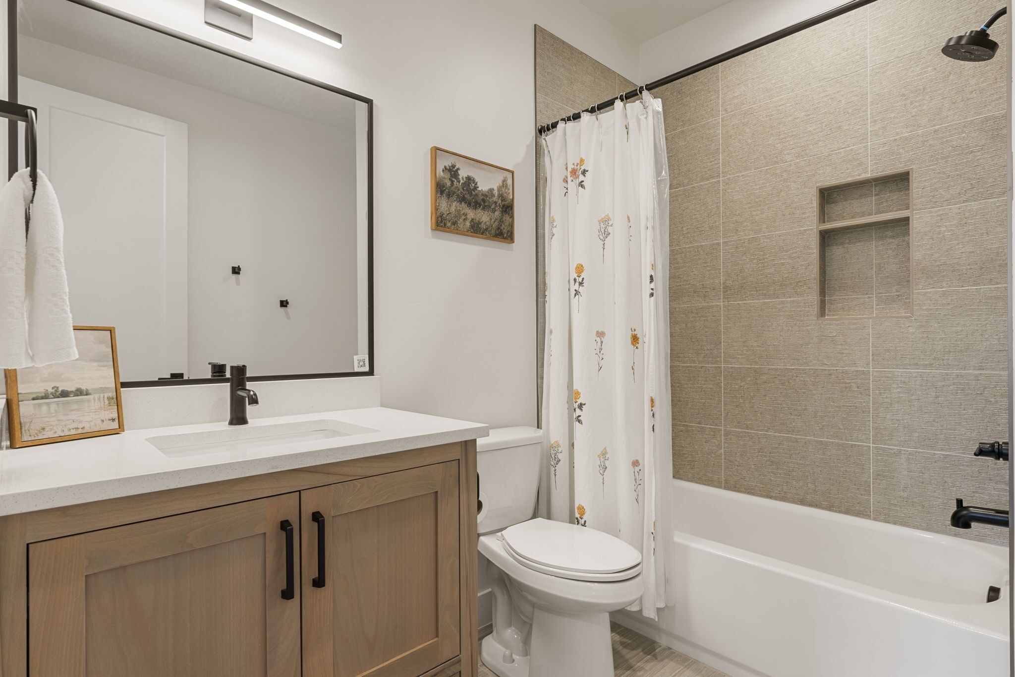 Un baño con lavamanos blanco, inodoro, bañera y cortina de ducha con motivos florales.