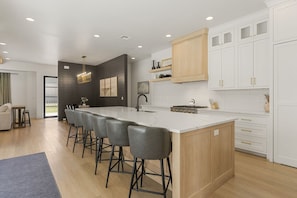 Una cocina moderna con una isla grande, taburetes de bar, armarios blancos y una lámpara colgante.