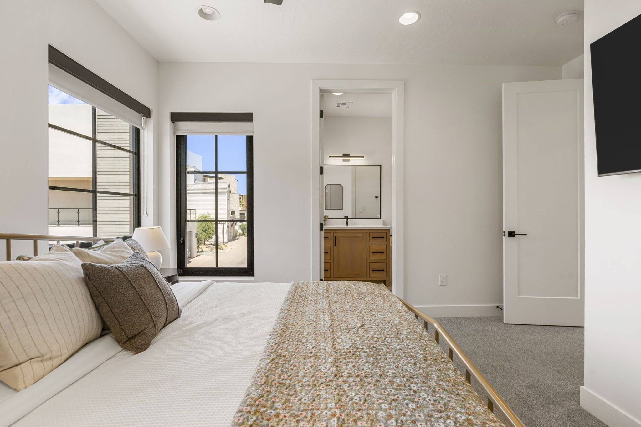 A bedroom with a bed, a window, a door, and a bathroom visible through an open door.