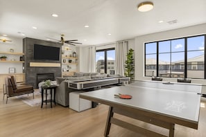 Una sala moderna con televisor de pantalla plana, chimenea, sofá y mesa de ping pong.