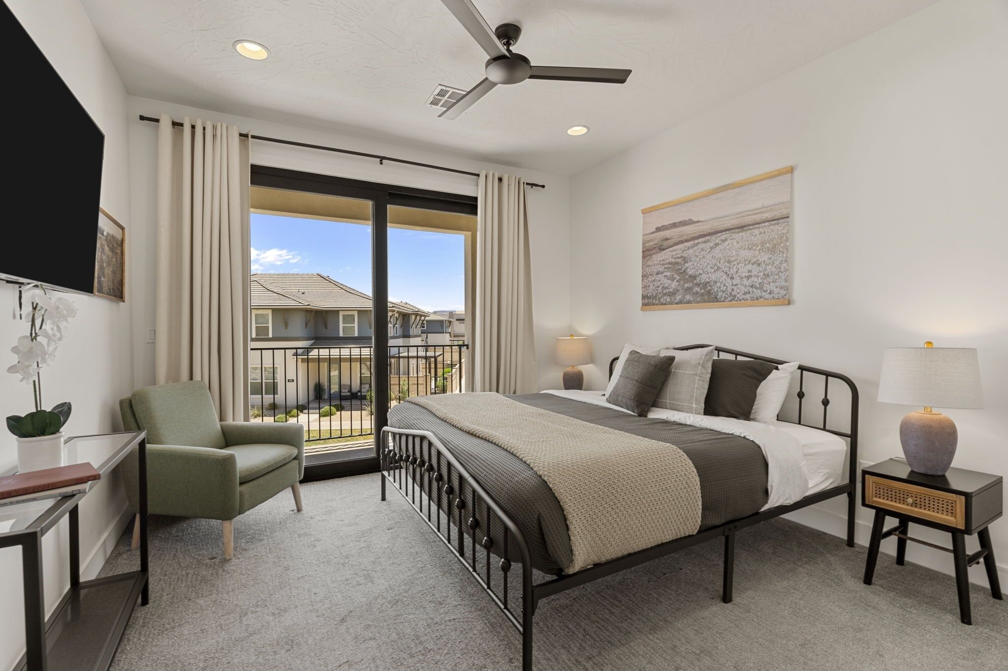 Quarto com cama, cadeira, escrivaninha, mesa de cabeceira, ventilador de teto e vista através de uma grande janela.