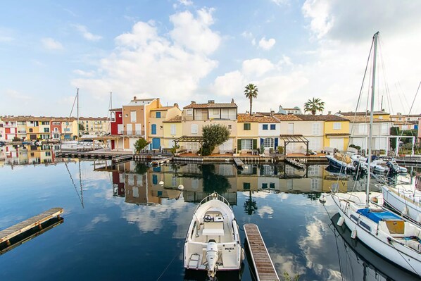 Un port de plaisance avec des bateaux amarrés, une jetée en bois et, au fond, des bâtiments aux couleurs vives.