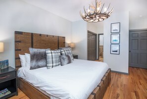 Ein Schlafzimmer mit einem Holz-Kopfteil, einem großen Bett mit weißer Bettwäsche, einer Chandelierleuchtre und gerahmten Bildern an der Wand.