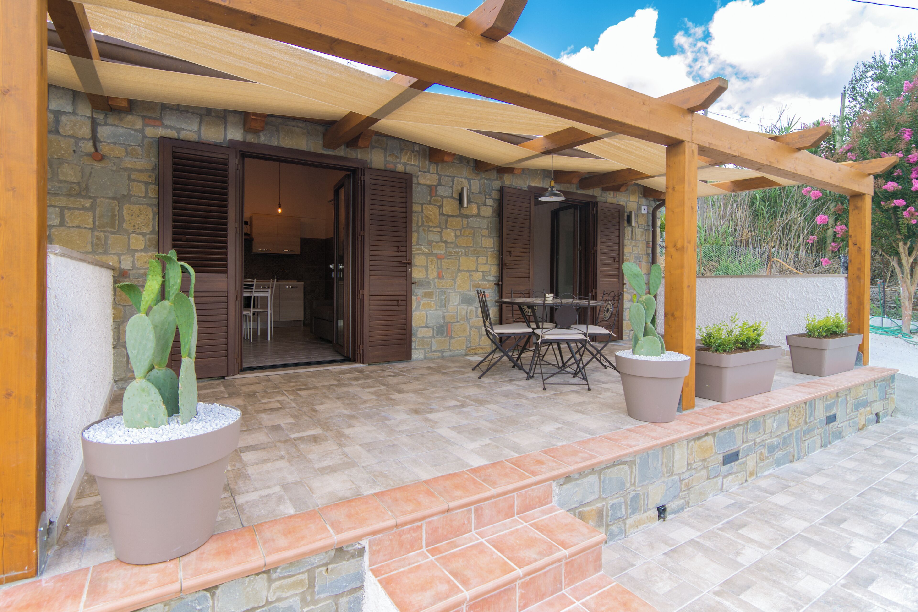 A patio area with a stone wall, wooden pergola, and potted plants.