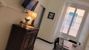 A room with a TV mounted on the wall, a dining table with chairs, a window with curtains, and a small cabinet with decorative items. - Ca' Sanlò2 confortable and near to Acquario of Genoa (Genova)