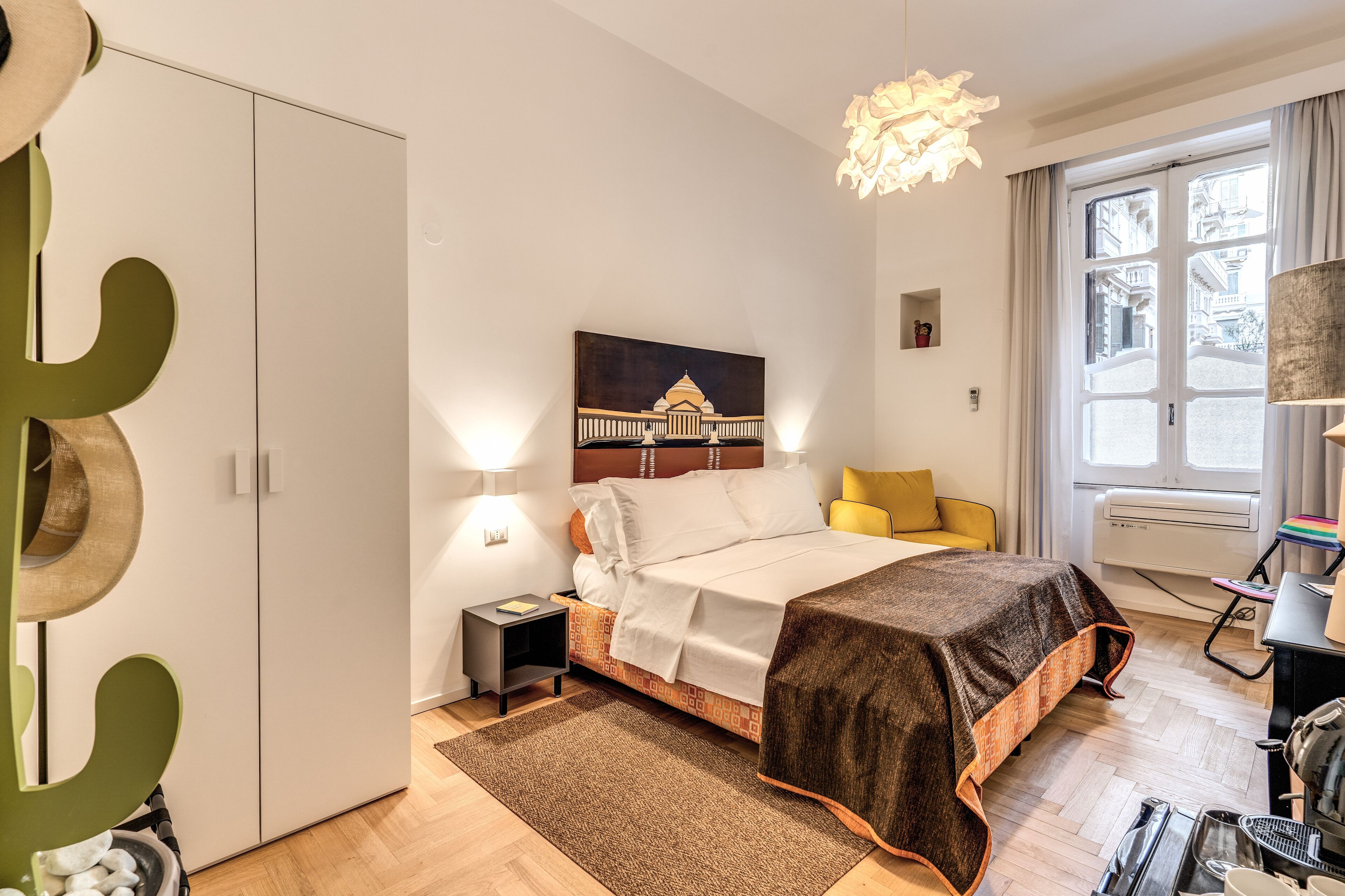 Une chambre moderne avec un lit, des tables de chevet, une commode, une lampe, une fenêtre avec des rideaux et une vue sur les bâtiments à l’extérieur.