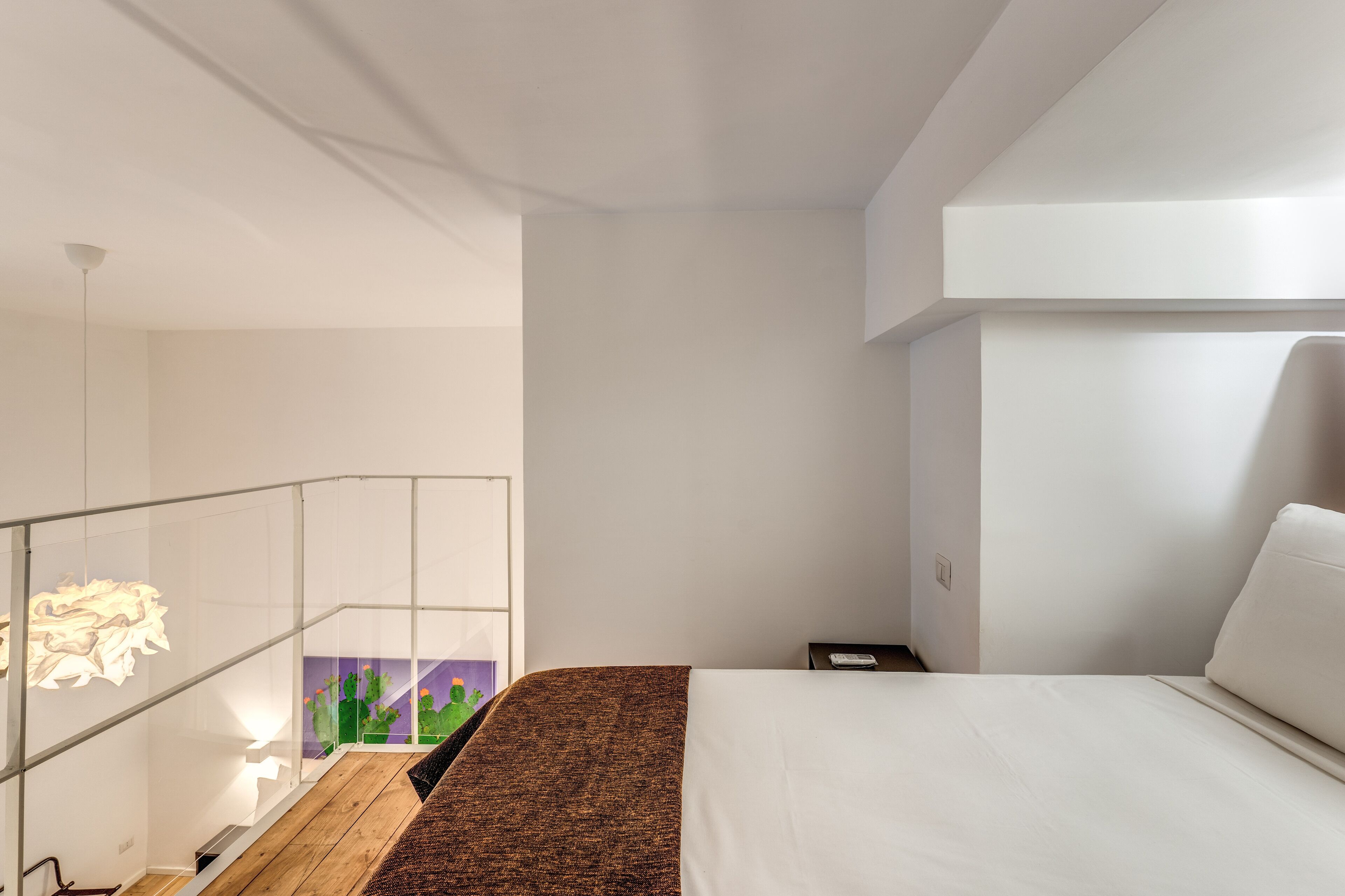Ett modernt hotellrum med en stor säng, ett glasräcke och utsikt över en kaktusträdgård.
