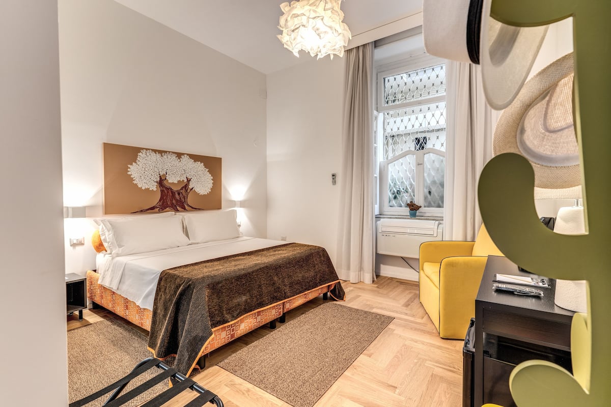 A hotel room with a bed, a desk, a chair, a window with curtains, and a decorative wall piece.