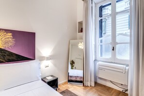 A hotel room with a bed, a nightstand, a mirror, a radiator, and a window with curtains. - La Corte di Partenope (Naples)