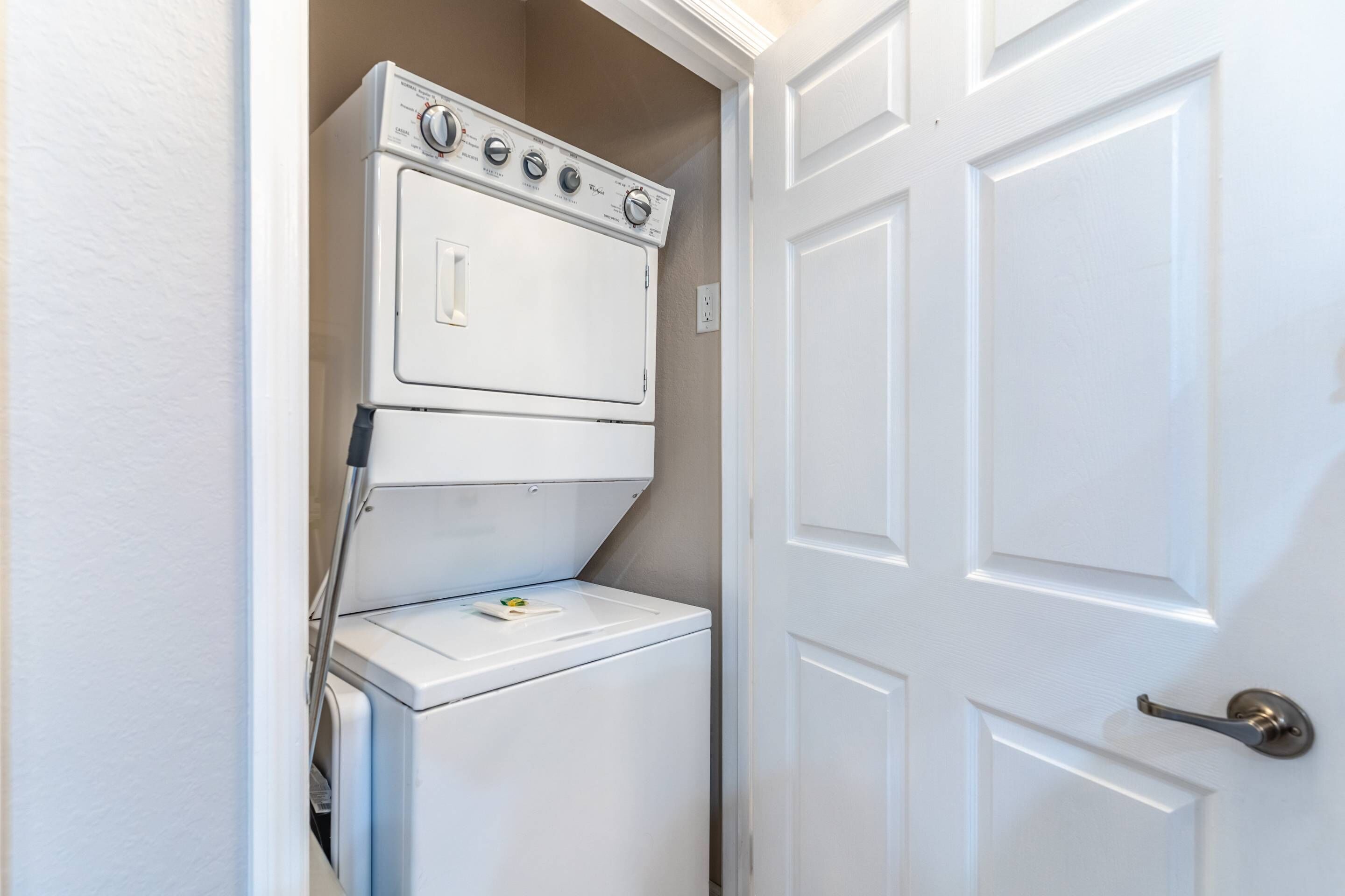 A compact laundry area with a stacked washer and dryer, a door with a silver handle, and a white wall.