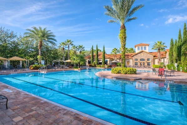 A swimming pool with lounge chairs and umbrellas, surrounded by palm trees and a building with a tiled roof. - 1301 Flamingo Cove at Tuscana (Davenport)