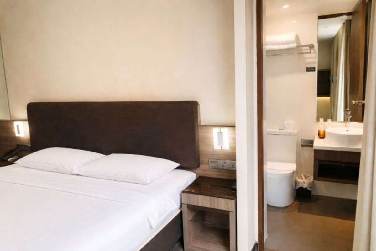 A hotel room with a bed, bedside table, and a bathroom with a toilet and sink.