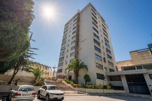 Un edificio alto de varios pisos con diseño moderno, que presenta una escalera central y un estacionamiento con dos coches.