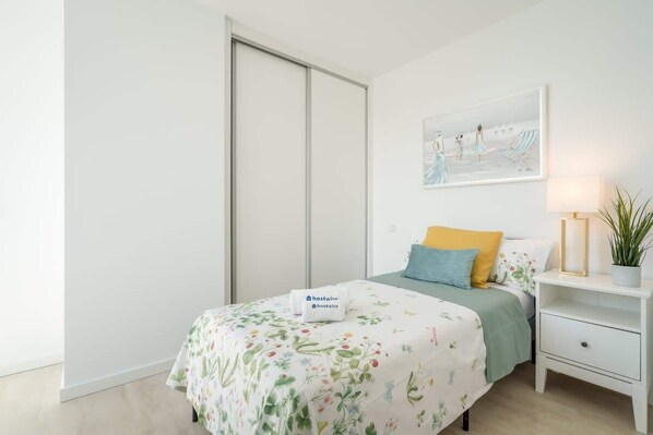 Un dormitorio con cama, mesita de noche, lámpara, cuadro y puerta corredera.