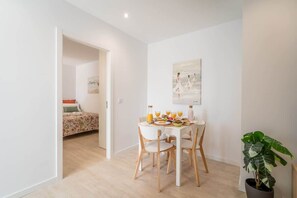 Un comedor con una mesa y sillas blancas, una planta en maceta y un cuadro en la pared.