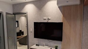 Una sala de estar moderna con un televisor de pantalla plana montado en la pared, un mueble empotrado debajo y un equipo de aire acondicionado en la pared.