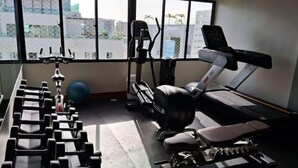 Un gimnasio con pesas, banca para press de banca, cinta de correr y bicicleta estática.