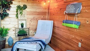 Une chambre chaleureuse aménagée dans un chalet en bois, avec un lit simple, une petite table agrémentée d’une plante et une fenêtre donnant sur un paysage agréable.