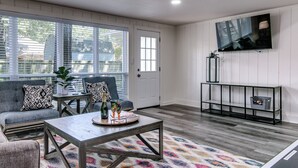Ein Wohnzimmer mit grauem Sofa, Couchtisch und Wandfernseher.