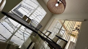 A modern dining area with a high ceiling, large windows with blinds, and a unique woven pendant light. - Convenient to Restaurants, Pool, Golf Views (Davenport)