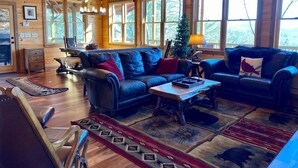 A cozy cabin interior with a wooden ceiling, large windows, a leather sofa, a coffee table, and a fireplace. - Stunning Views From Lodge, and With hot Tub! (Blue Ridge)