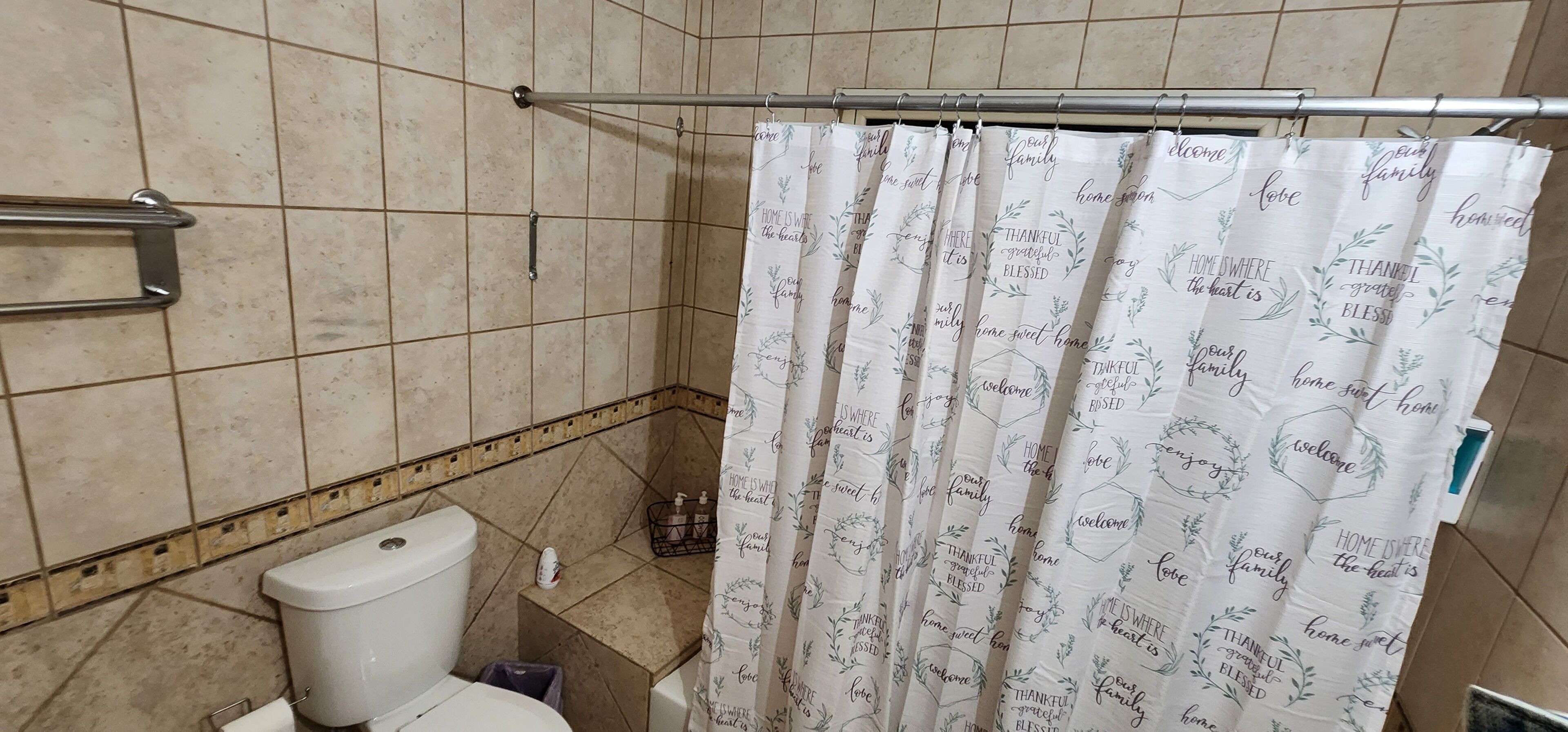 A bathroom with a shower curtain featuring home-related phrases, a toilet, and a towel rack.