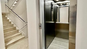 Un ascensore moderno con finitura metallica, una scala con corrimano bianchi e un tappeto decorato sul pavimento.