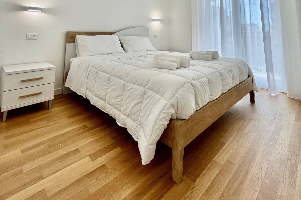 A modern bedroom with a wooden bed, white bedding, a nightstand, and a ceiling light fixture.