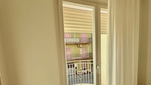 Una stanza con una porta a vetri scorrevoli che dà su un balcone con ringhiera metallica.