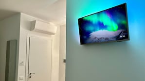 Una stanza con una TV a parete che mostra l'aurora boreale, una porta bianca e un condizionatore d'aria a soffitto.