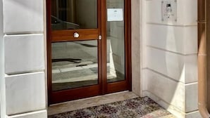 L'ingresso di un edificio con una porta in legno, un tappetino d'ingresso piastrellato e il numero '2A' sulla parete.