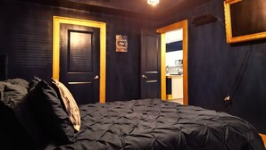 A bedroom with a dark-colored bed, two doors, a chandelier, and a kitchen visible through an open door. - Live Like ROYALTY in Buckhead This unique place has a style all of its own. (Atlanta)