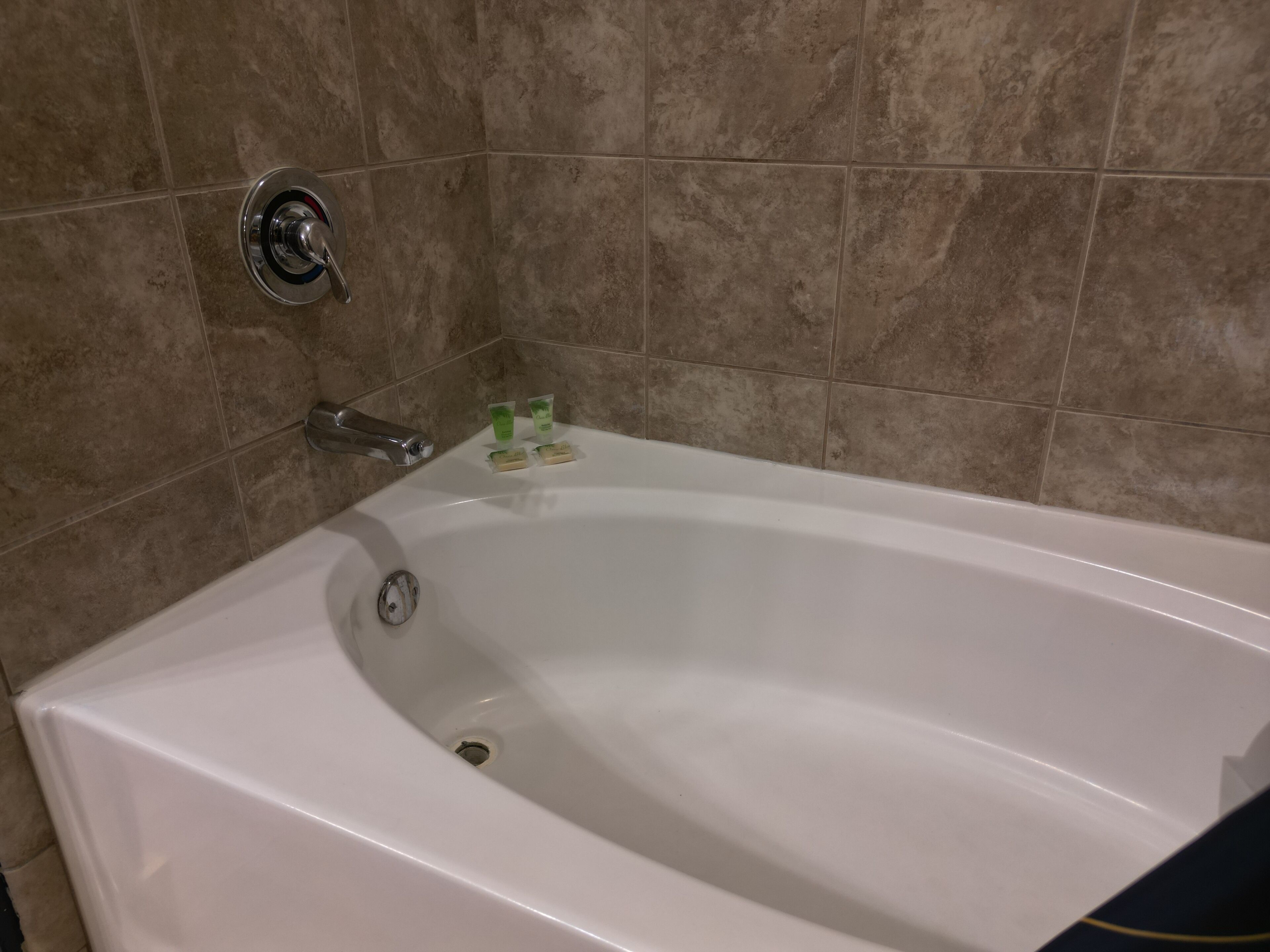 A white bathtub with a chrome faucet and a drain, set against beige tiled walls.