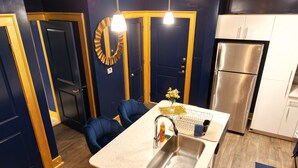 A compact kitchen with a sink, a stainless steel refrigerator, and blue chairs. - Live Like ROYALTY in Buckhead This unique place has a style all of its own. (Atlanta)
