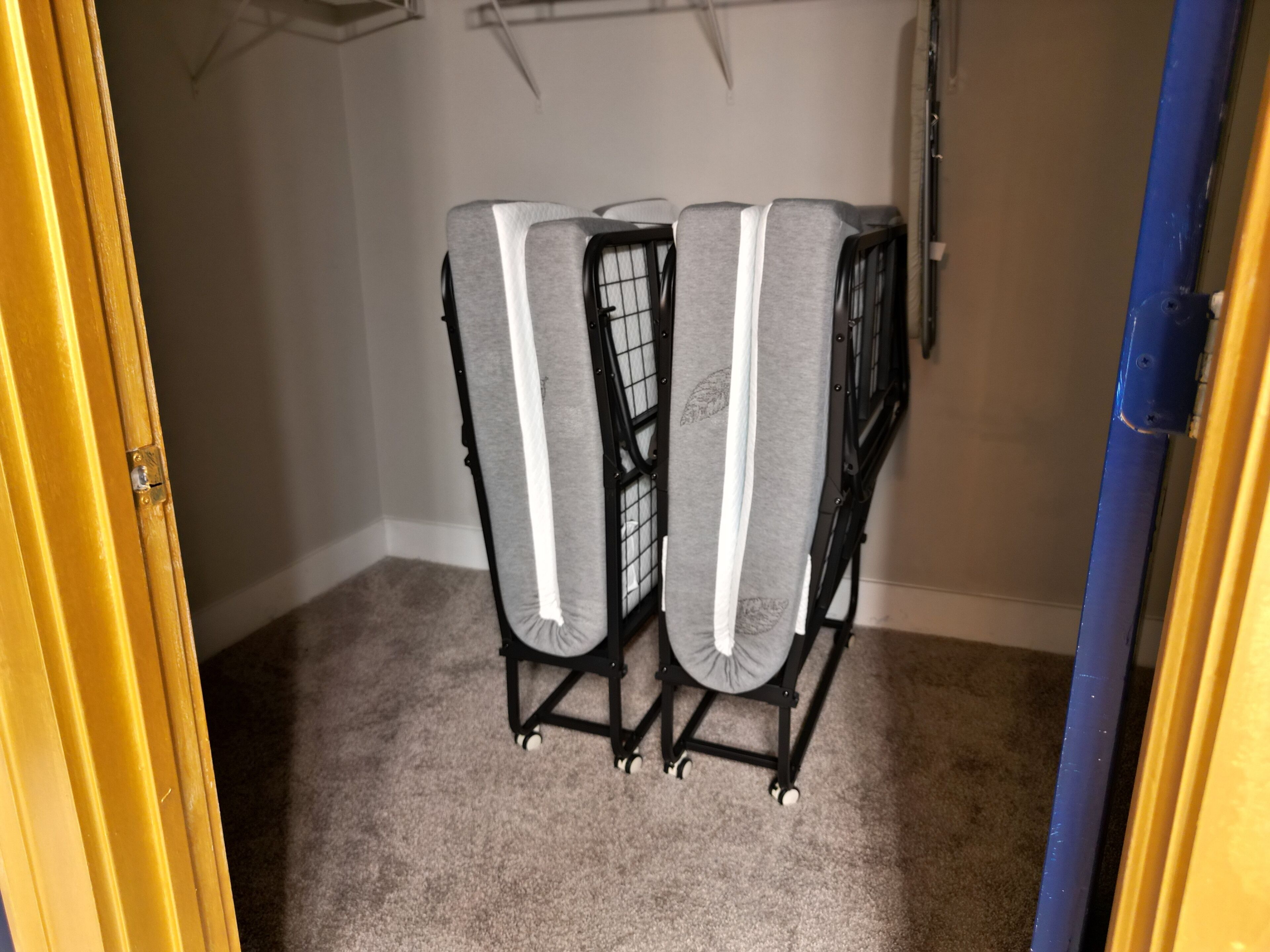 A room with a grey carpet, a black metal rack with white straps, and a wooden door.