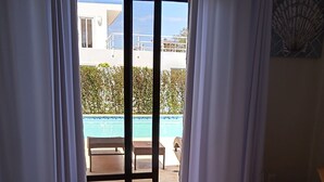 Une chambre dotée d’un grand lit, offrant une vue sur une piscine, et comprenant un espace patio avec une table et des chaises.