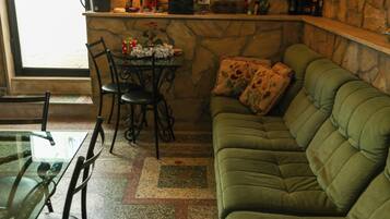 A cozy living area with a green sofa, a dining table with chairs, and a stone wall with a chandelier.
