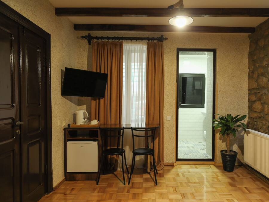 Una habitación compacta con suelo de madera, una pequeña mesa con sillas, un televisor montado en la pared, una planta en maceta y una pared de piedra.