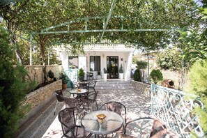 An outdoor patio with tables and chairs, a stone wall, and a white building in the background. - Hotel History (Kutaisi)