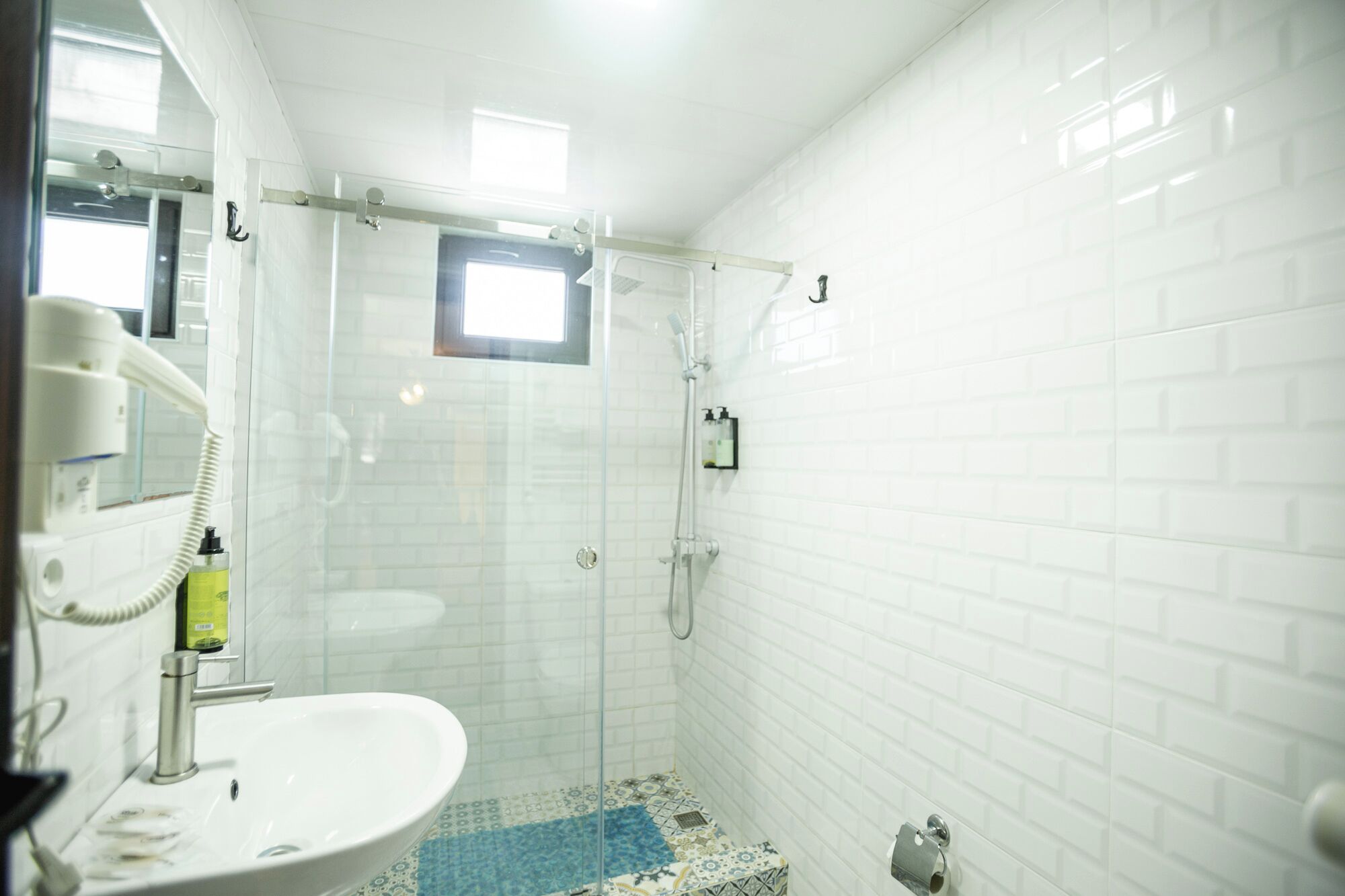 Un baño con un lavamanos blanco, cabina de ducha con mampara de vidrio y un ventanal pequeño.