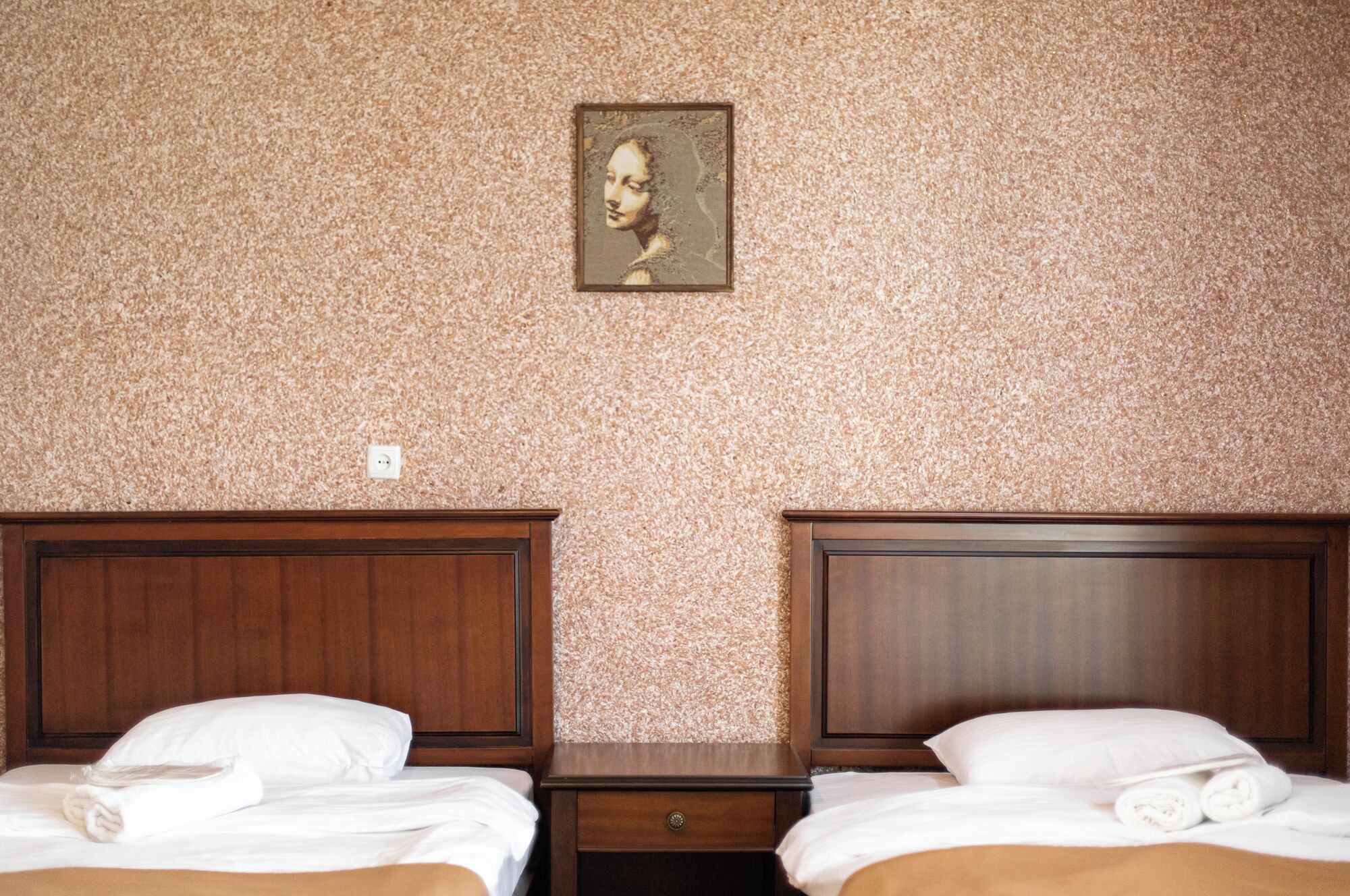 A hotel room with two wooden beds, a small nightstand, and a textured wall.