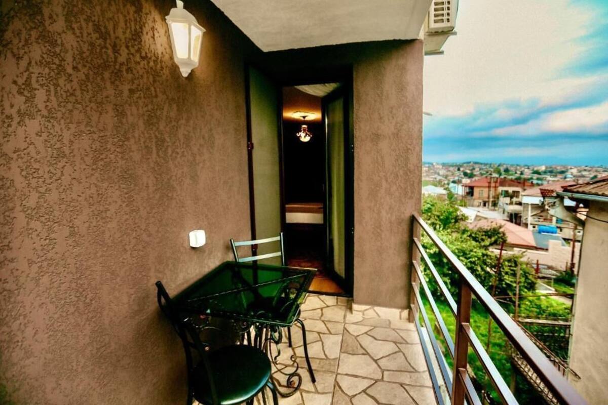 A balcony with a table and chairs, a view of the city, and a door leading to an interior space.