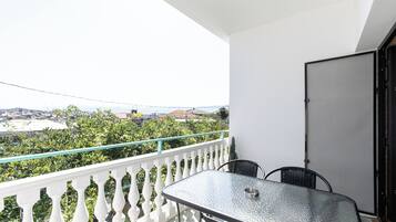 Ein Balkon mit Glastisch und -stühlen, weißem Geländer und Blick auf eine Stadtlandschaft.